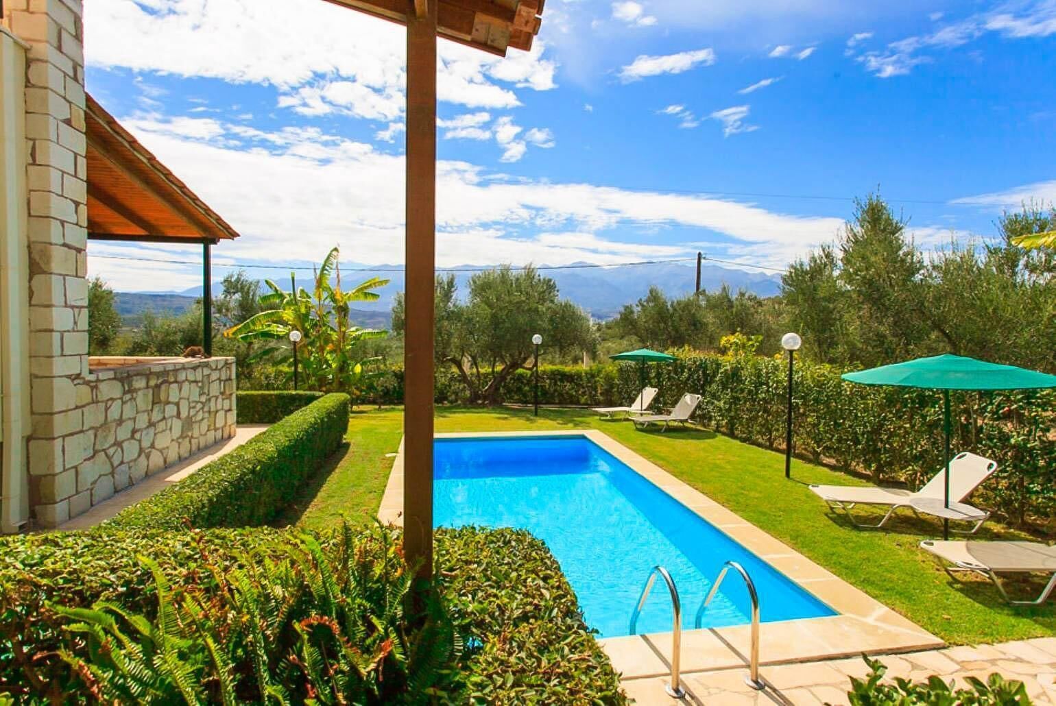 A swimming pool with a pergola, lounge chairs, and a stone wall.