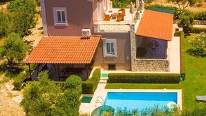 Ein zweistöckiges Haus mit Swimmingpool, umgeben von Olivenhainen und einem Berg im Hintergrund.