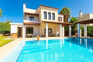 Una casa a due piani con piscina, area salotto esterna e giardino.