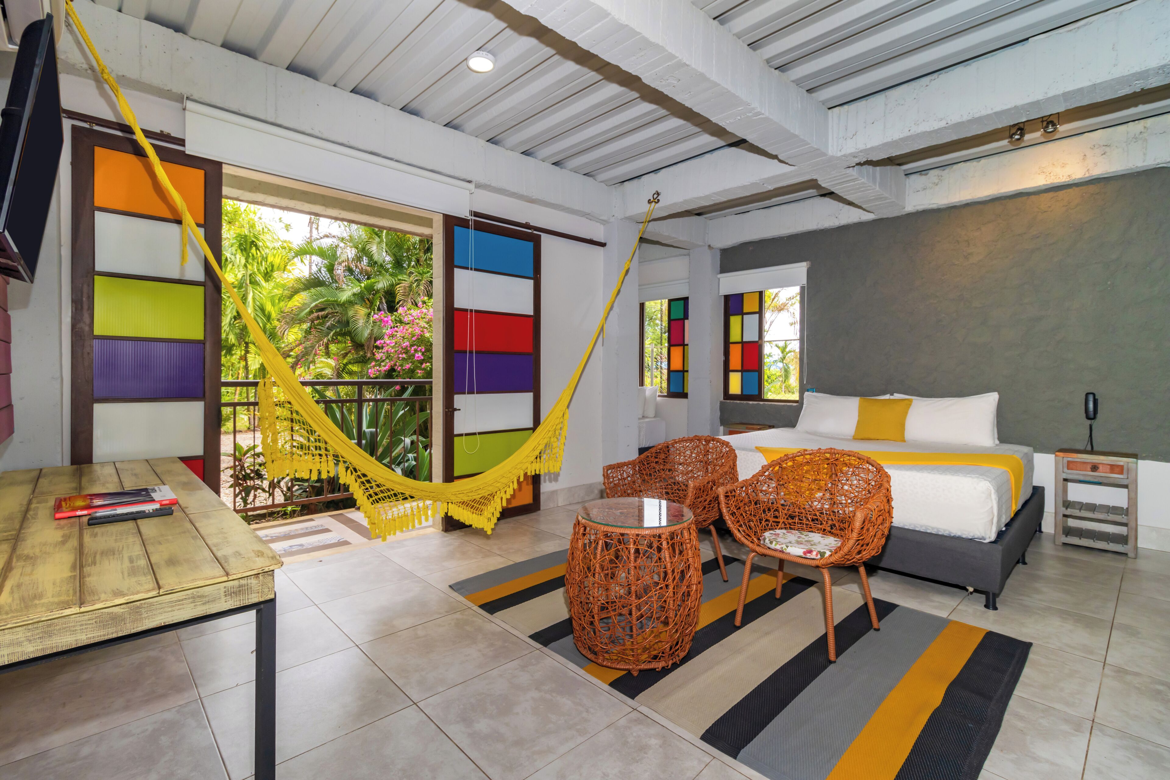 A room with a bed, two wicker chairs, a small table, and a hammock.