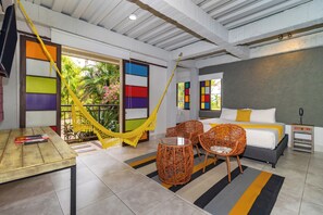 Una habitación con una cama, dos sillones de mimbre, una mesita y una hamaca.