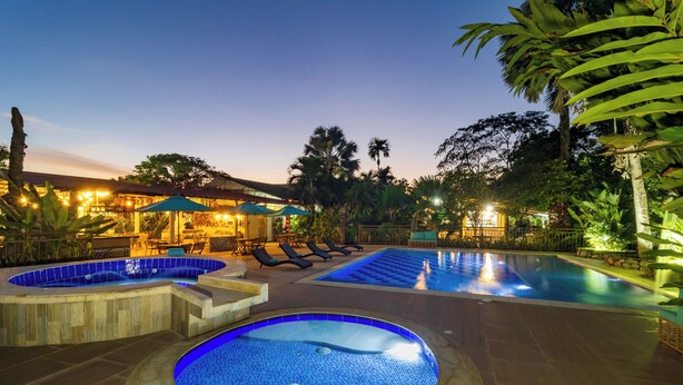 A pool area with hot tubs and lounge chairs, surrounded by tropical plants and evening lighting. - NQ Hotel Orinoquía (Villavicencio)