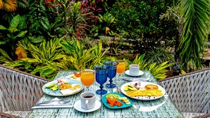 An outdoor dining table set with plates of food, drinks, and cutlery, surrounded by lush greenery. - NQ Hotel Orinoquía (Villavicencio)