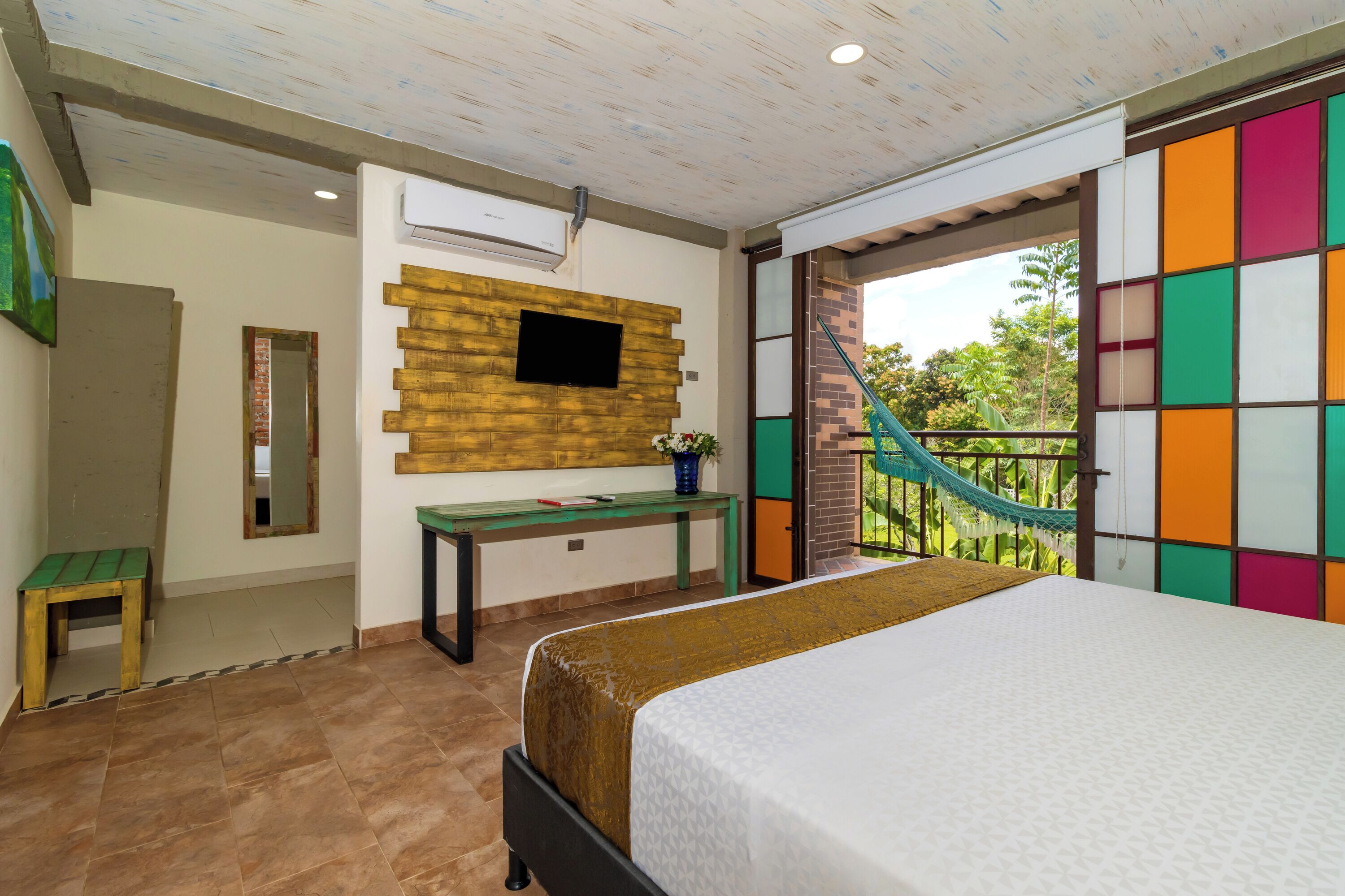 A bedroom with a bed, a TV mounted on a wooden wall, a small table, and a bench.