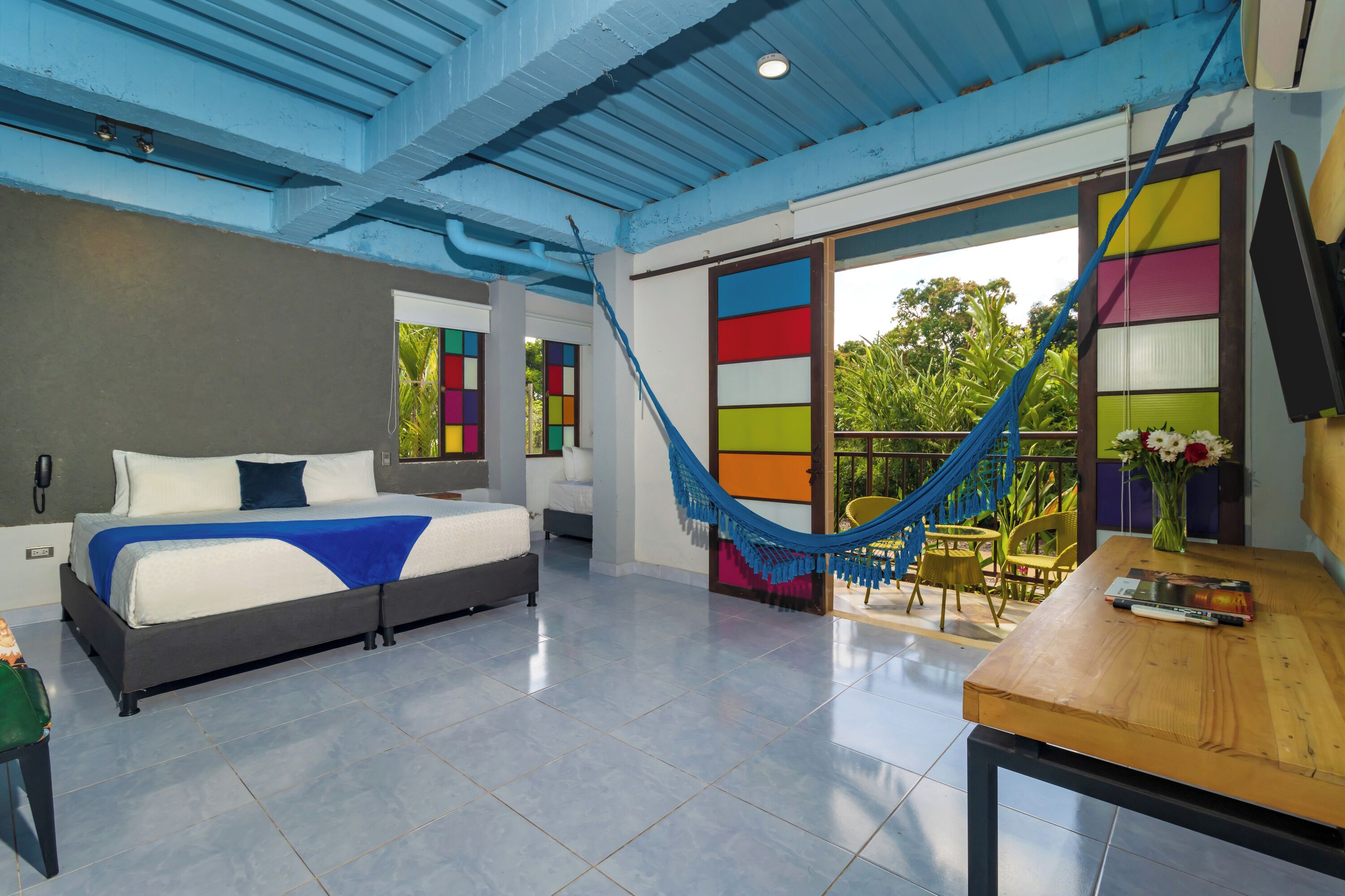 Una habitación de hotel moderna con cama, hamaca, mesa de comedor y vistas a la vegetación.