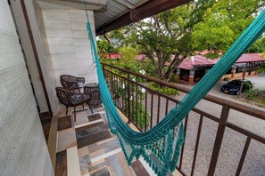 Un balcon avec un hamac, des fauteuils en osier et une vue sur un immeuble avec un toit rouge.