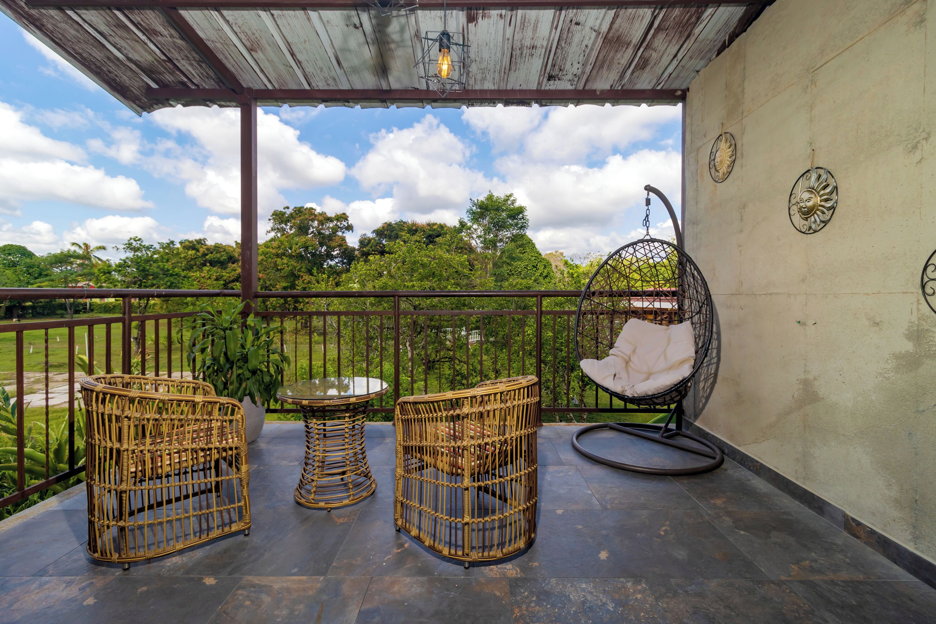 A covered outdoor seating area with wicker furniture, a hanging chair, and decorative wall plates.
