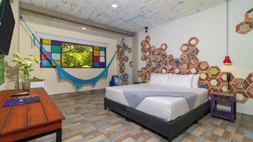 Un dormitorio con cama, una mesa de madera, una hamaca y una ventana con vistas a árboles.
