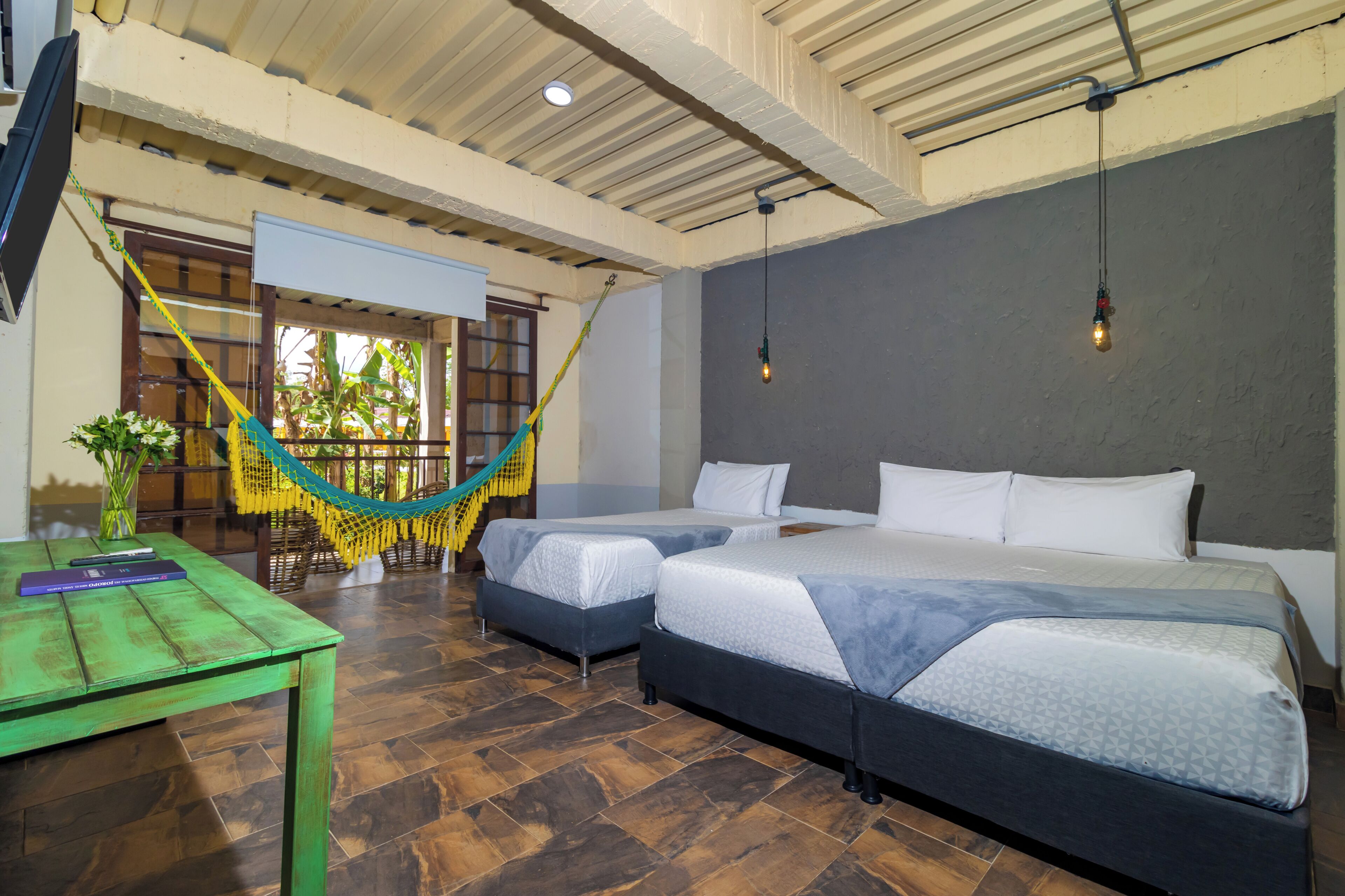 A room with two beds, a hammock, a table with a vase, and a ceiling fan.