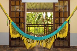 A hammock suspended between two glass doors, with a view of a garden and a wooden ceiling.
