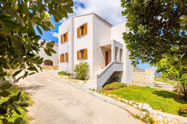 Un bâtiment blanc avec des volets en bois, un chemin de pierre et une vue sur la mer.