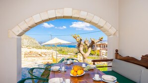 Un comedor con una mesa dispuesta para dos, con vistas a un paisaje marino y un árbol.