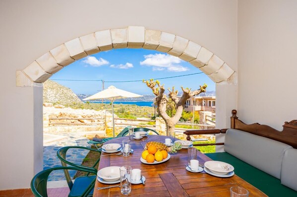 A dining area with a table set for two, overlooking a scenic view of the sea and a tree. - Villa Neria - Four Bedroom Villa, Sleeps 8 (Aptera)