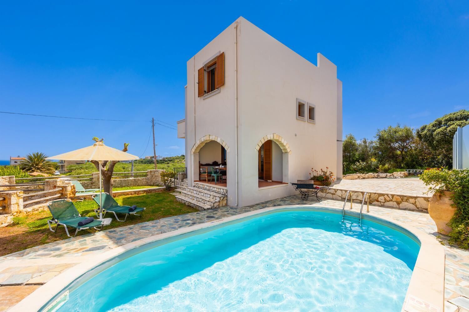 A modern villa with a swimming pool, outdoor seating, and a stone pathway.