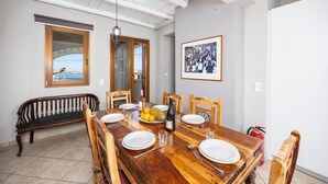 Un comedor con una mesa de madera dispuesta para seis comensales, un banco y un cuadro en la pared.