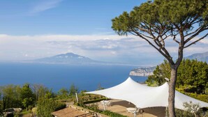 A scenic outdoor area with a white canopy, wooden deck, and a large tree. - Elegant Sorrento Coast Villa with Pool and Tennis Court (Massa Lubrense)
