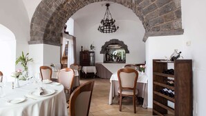 A dining area with brick arches, white tables, and chairs. There is a wine rack and a chandelier. - Elegant Sorrento Coast Villa with Pool and Tennis Court (Massa Lubrense)