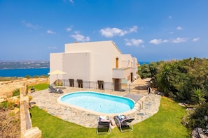 Ett modernt hus med en swimmingpool, omgivet av en stenbelagd uteplats och med utsikt över havet.