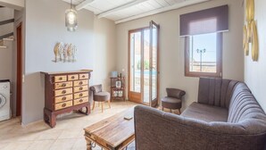Un salon spacieux avec une table basse en bois, un canapé et un meuble avec des tiroirs. Il y a une fenêtre donnant sur l’extérieur et une porte menant à une autre pièce.