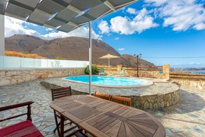 A pool area with stone flooring, a wooden table, and a lounge chair.