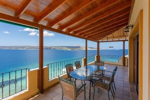 A covered outdoor area with a table and chairs, overlooking a coastal view. - Souda Bay View - Five Bedroom Villa, Sleeps 12 (Kalami)