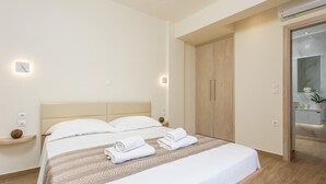 Una habitación de hotel moderna con una cama grande, un armario de madera y un baño visible a través de una puerta de cristal.
