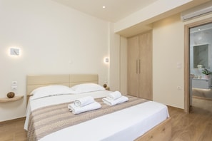 Moderni hotellihuone, jossa on suuri sänky, puinen vaatekaappi ja kylpyhuone, joka on näkyvissä lasiovesta.