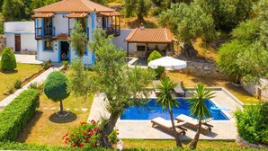 Una casa de dos plantas con piscina, rodeada de vegetación y árboles.