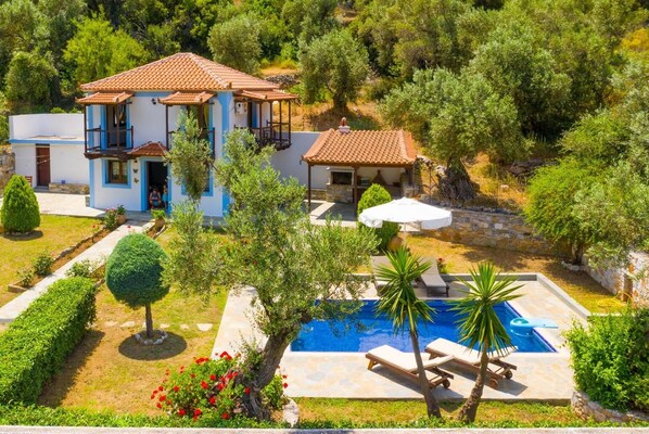 A two-story house with a swimming pool, surrounded by greenery and trees.