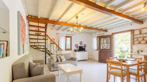 Amplia sala de estar con una escalera, una mesa de comedor con sillas, un sofá y una zona de cocina con ventanal.