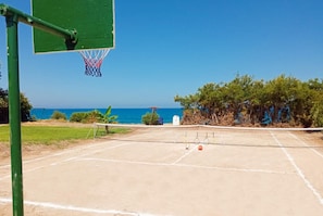 Un court de tennis en plein air, équipé d’un filet, d’un panier de basket et offrant une vue sur la mer.