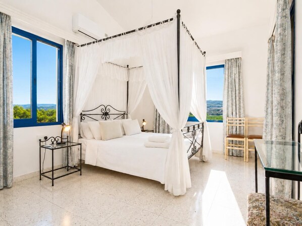 Un lit à baldaquin, une table de chevet avec une lampe, une chaise et une vue sur le paysage par les fenêtres.