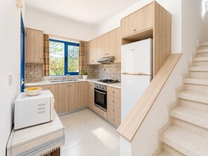 A compact kitchen with wooden cabinets, a gas stove, a sink, and a white refrigerator.