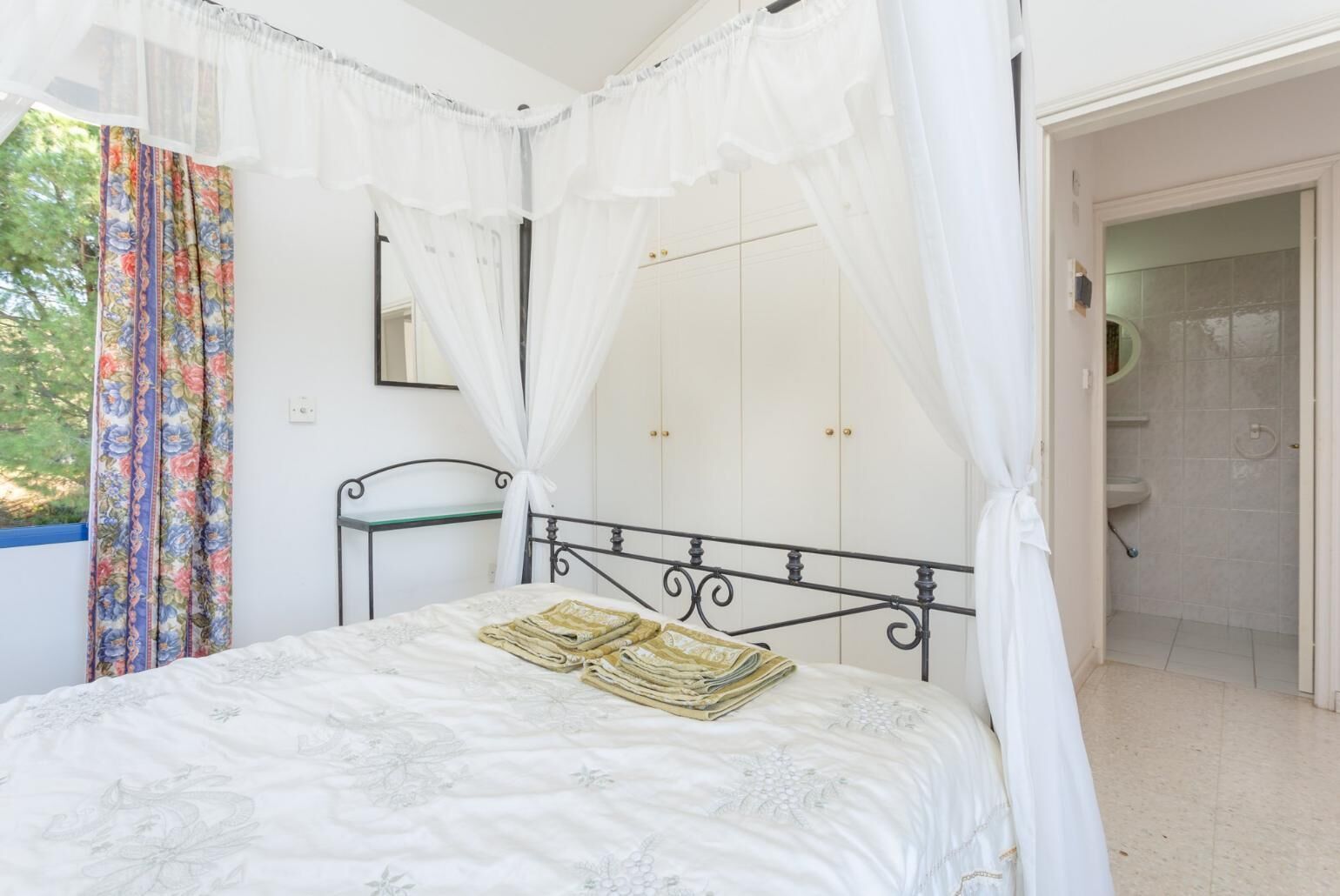 A bedroom with a bed, a bedside table, a wardrobe, and a bathroom visible through an open door.