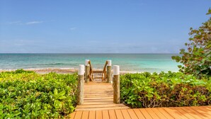 Un sentier en bois mène à une plage où l’eau est d’un bleu turquoise éclatant et le ciel est dégagé.