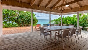 Un espace extérieur abrité doté d’une terrasse en bois, d’une table avec des chaises et d’une vue sur l’océan.
