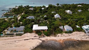 Vue aérienne d’un quartier résidentiel situé sur la côte, avec des maisons entourées d’une végétation luxuriante et une plage.