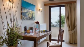 Zona de menjador amb taula de fusta, llibres, un ordinador portàtil i un ram de flors. Hi ha un quadre a la paret i vistes cap a l'exterior a través d'una finestra.