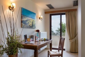 Un coin repas avec une table en bois, des livres, un ordinateur portable et un vase de fleurs. Un tableau orne le mur et une fenêtre offre une vue sur l’extérieur.
