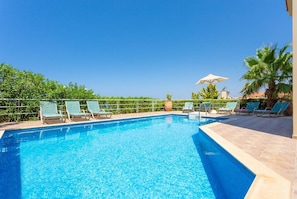 Piscina azul cristalina com espreguiçadeiras e guarda-sóis, em meio à vegetação e palmeiras.
