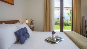 Habitació d'hotel amb un llit, una bandeja amb tasses i un vas, una nitòria amb una làmpada, i una finestra amb cortines.