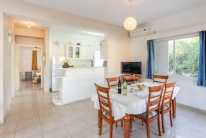 A modern kitchen with white cabinets, a dining table with wooden chairs, and a TV in the corner.