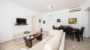 Ett modernt vardagsrum med en soffa, ett soffbord, en tv och en matplats med ett bord och stolar.