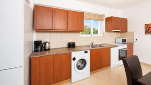 Een compacte keuken met houten kastjes, een wasmachine, een magnetron en een koffiezetapparaat.
