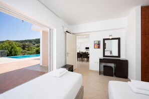 Ein Hotelzimmer mit Bett, Schreibtisch, Stuhl, Spiegel und Blick auf Pool und Grünfläche.
