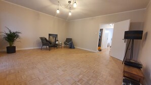 A spacious room with a herringbone parquet floor, two wicker chairs, a small table, a potted plant, and a ceiling light fixture. - matejki apartament (Poznan)