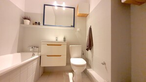 A compact bathroom with a white bathtub, a white toilet, and a mirror above the sink. - matejki apartament (Poznan)