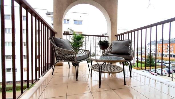 A balcony with wicker furniture, a glass table, and potted plants. - matejki apartament (Poznan)