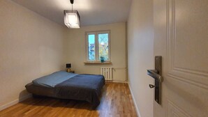 A small, well-lit bedroom with a bed, a window with a view, and a radiator. - matejki apartament (Poznan)