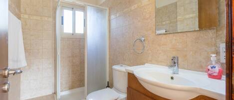 A bathroom with a shower, toilet, sink, and a mirror.